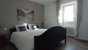 A bedroom with a bed, a nightstand, a lamp, a window with curtains, and a painting on the wall.