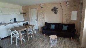 A compact living space with a kitchenette, a dining table with chairs, a black sofa with blue cushions, and a small round coffee table.