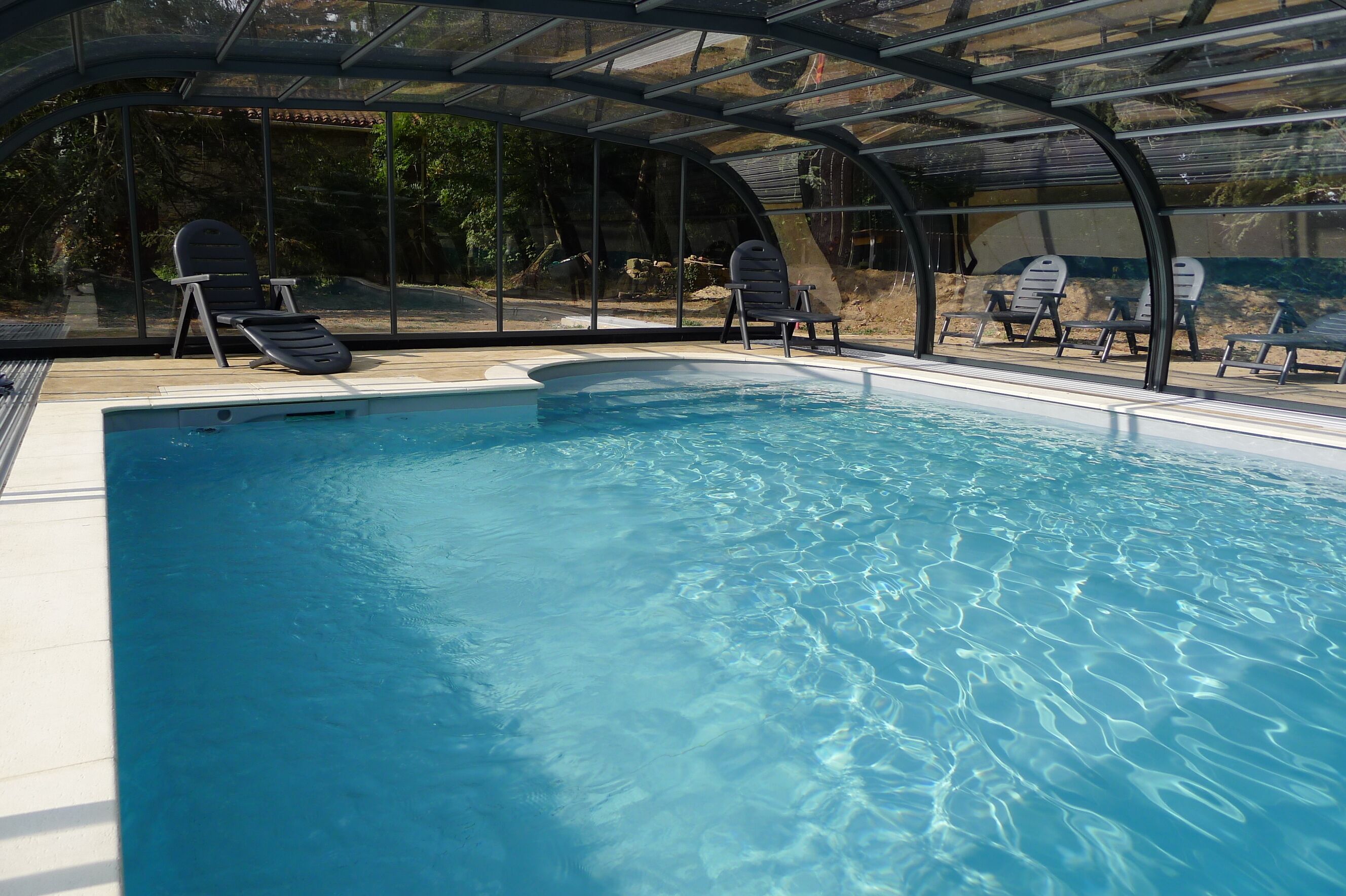 A swimming pool with clear blue water, surrounded by lounge chairs and a glass-enclosed roof.