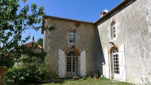 Un edificio rústico de piedra con un arco central, flanqueado por dos ventanas con contraventanas, y un pequeño balcón.