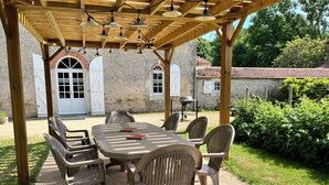 Un patio exterior con una pérgola de madera, una mesa redonda y seis sillas.