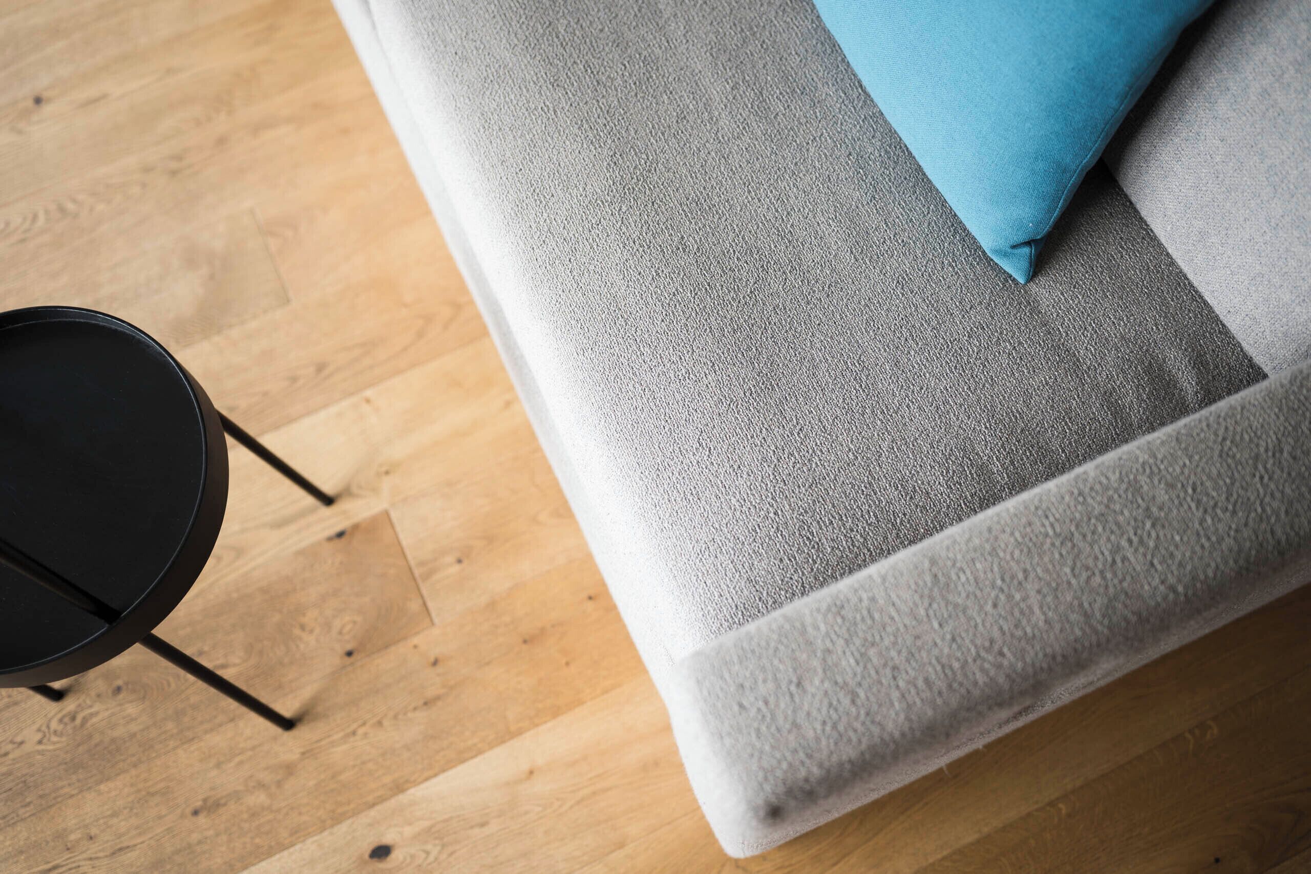 A grey sofa with a blue pillow, a black round table, and wooden flooring.