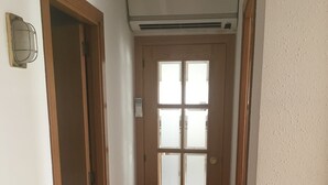 A hallway with a wooden door, a window, and an air conditioning unit. - Apartment 150 m beach with garden and garage (llança)