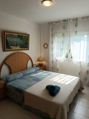 Une chambre à coucher avec un lit, une table de chevet avec une lampe, un tableau au mur et une fenêtre avec des rideaux.
