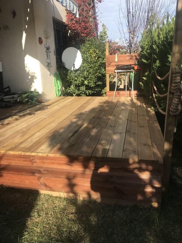 A wooden deck with a small wooden structure, surrounded by greenery and a satellite dish.