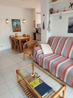 Ein Wohnzimmer mit Sofa, Couchtisch mit Büchern, Essbereich mit Stühlen und Wanddekorationen.
