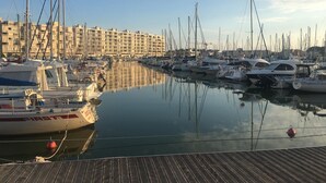 En småbåtshamn med flera båtar förtöjda, en träbrygga och en stor byggnad i bakgrunden.