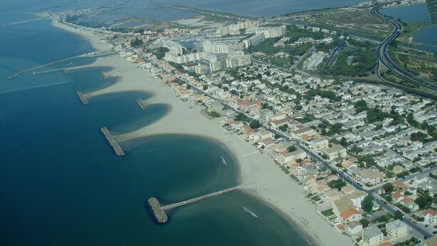 Ett flygbildsfoto av en kuststad med en strand, bostadsområden och en bro som förbinder två landområden.