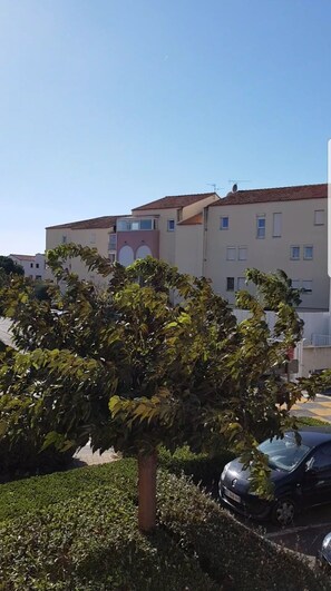 A residential building with multiple windows and balconies, surrounded by greenery and parked cars.