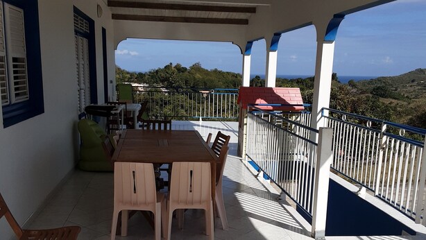 A covered patio with a wooden table and chairs, a tiled floor, and a view of the landscape. - Villa between sea and countryside (Le Marin)