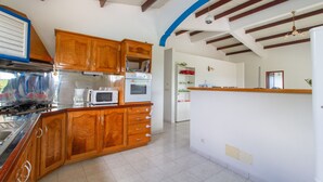 A kitchen with wooden cabinets, a microwave, an oven, and a gas stove. - Villa between sea and countryside (Le Marin)