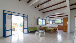 A spacious living area with a sofa, a coffee table, and a dining table with chairs. There is a kitchen area with wooden cabinets and a refrigerator. - Villa between sea and countryside (Le Marin)