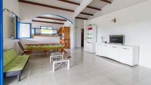 A spacious living room with a sofa, a dining table, a TV, and a white cabinet. - Villa between sea and countryside (Le Marin)