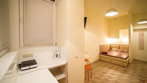 Una habitación pequeña con cama, una mesita, una silla y ventana con persianas.