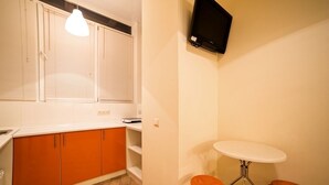 Una cocina compacta con gabinetes naranjas, una encimera blanca, una mesa redonda y dos taburetes naranjas.