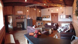 Un interior rústico con paredes de madera, una chimenea, un televisor y una zona de comedor con mesa y sillas.