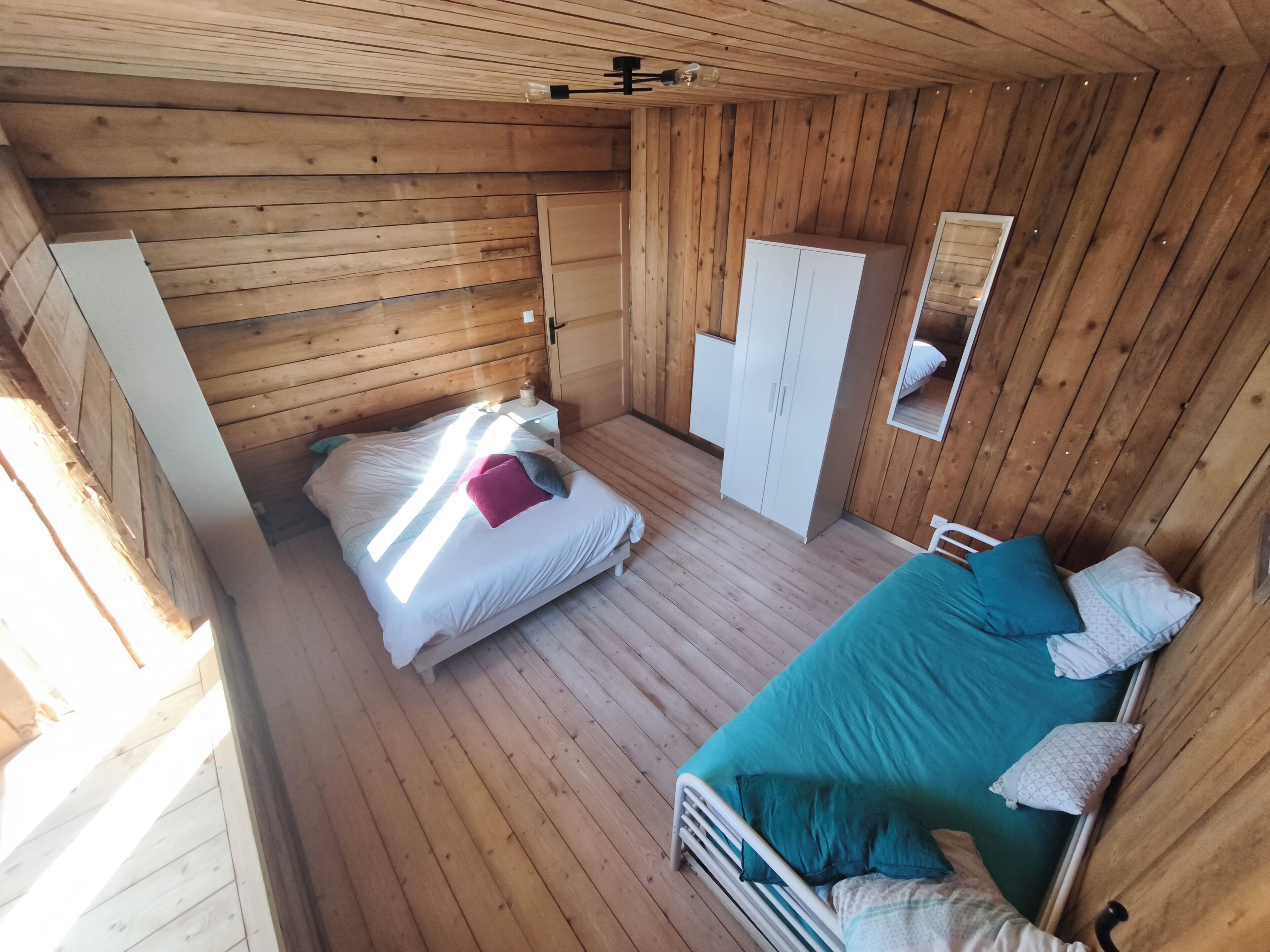 A wooden cabin bedroom with a single bed, a wardrobe, and a mirror.