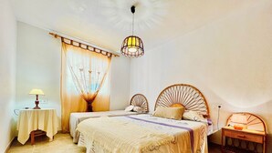 A bedroom with two single beds, a bedside table with a lamp, a decorative hanging light, and a small table with a lamp.