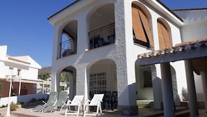 A two-story building with a white exterior, multiple balconies, and a covered outdoor seating area with chairs.