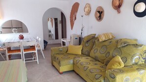 A living room with a yellow patterned sofa, a striped area rug, and a dining table with chairs.