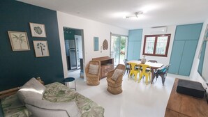 A living room with a sofa, chairs, a dining table, and a kitchen area. - Banan'appart - the magnificent Hermitage T3 with fully renovated garden (L'Ermitage-Les-Bains)
