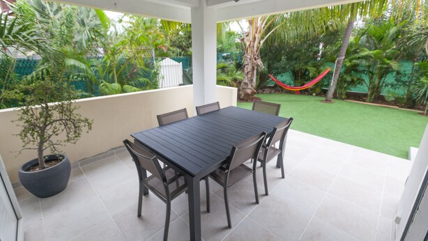 A covered patio with a dining table and chairs, surrounded by a lush garden and a hammock. - Banan'appart - the magnificent Hermitage T3 with fully renovated garden (L'Ermitage-Les-Bains)