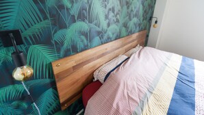 A bedroom with a wooden headboard, a patterned wall, a bedside lamp, and a striped bedspread. - Banan'appart - the magnificent Hermitage T3 with fully renovated garden (L'Ermitage-Les-Bains)