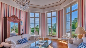 A spacious living room with a large window, a chandelier, and striped wallpaper.