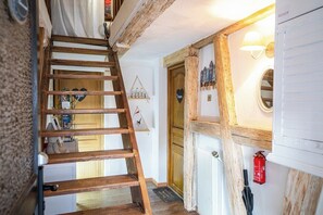 Puiset portaat johtavat huoneeseen, jossa on puinen ovi, valkoinen patteri ja seinään kiinnitetty valaisin.