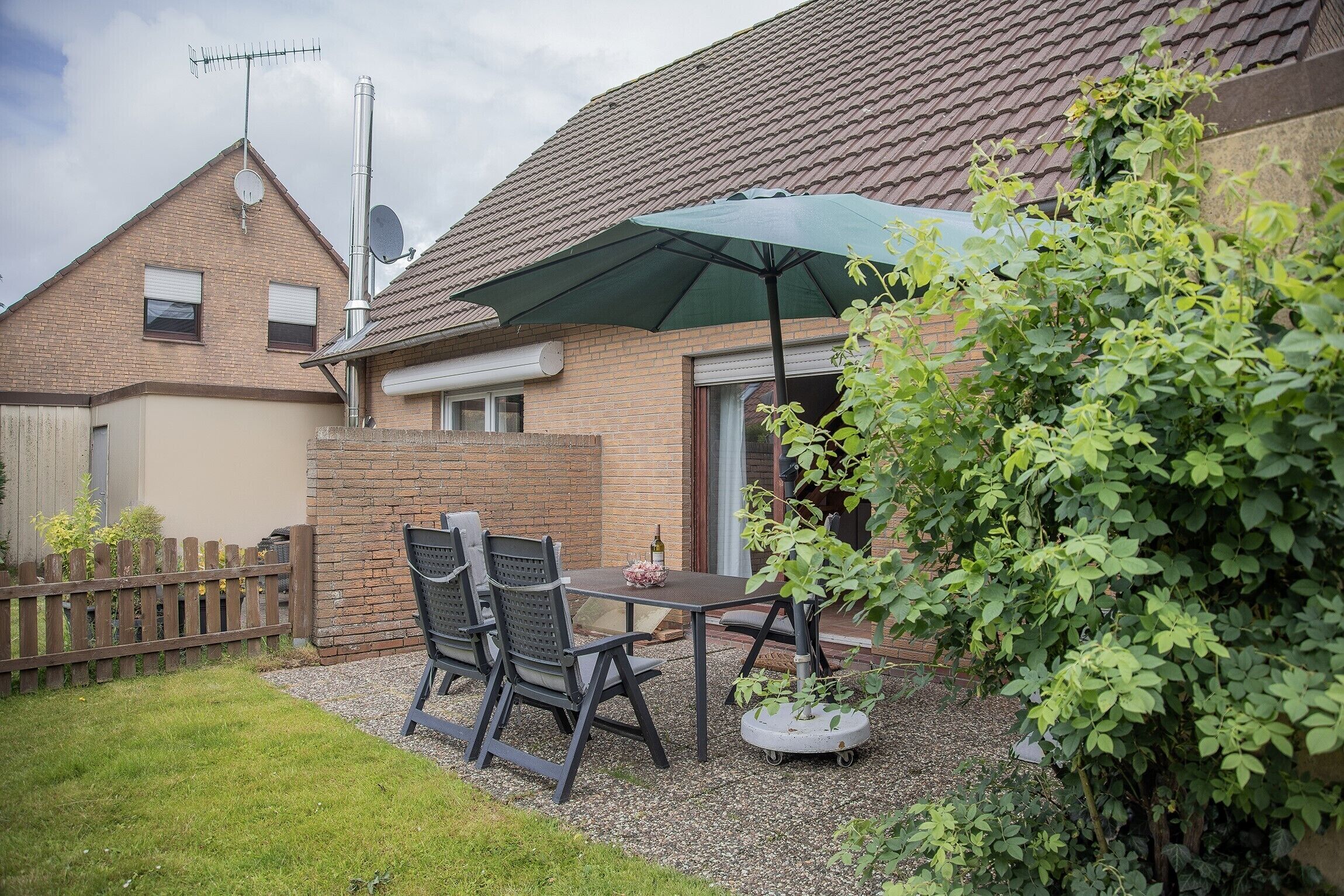 Eine Terrasse mit Tisch und Stühlen, einem Blumentopf und einem Ziegelhaus mit Ziegeldach.