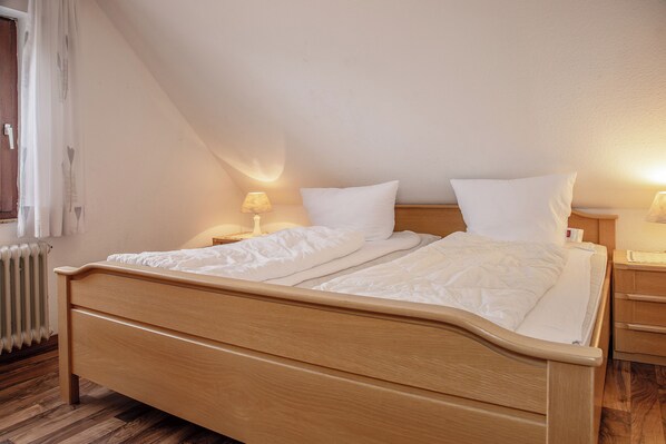 A neatly made bed with white linens in a room with wooden flooring and a sloped ceiling.