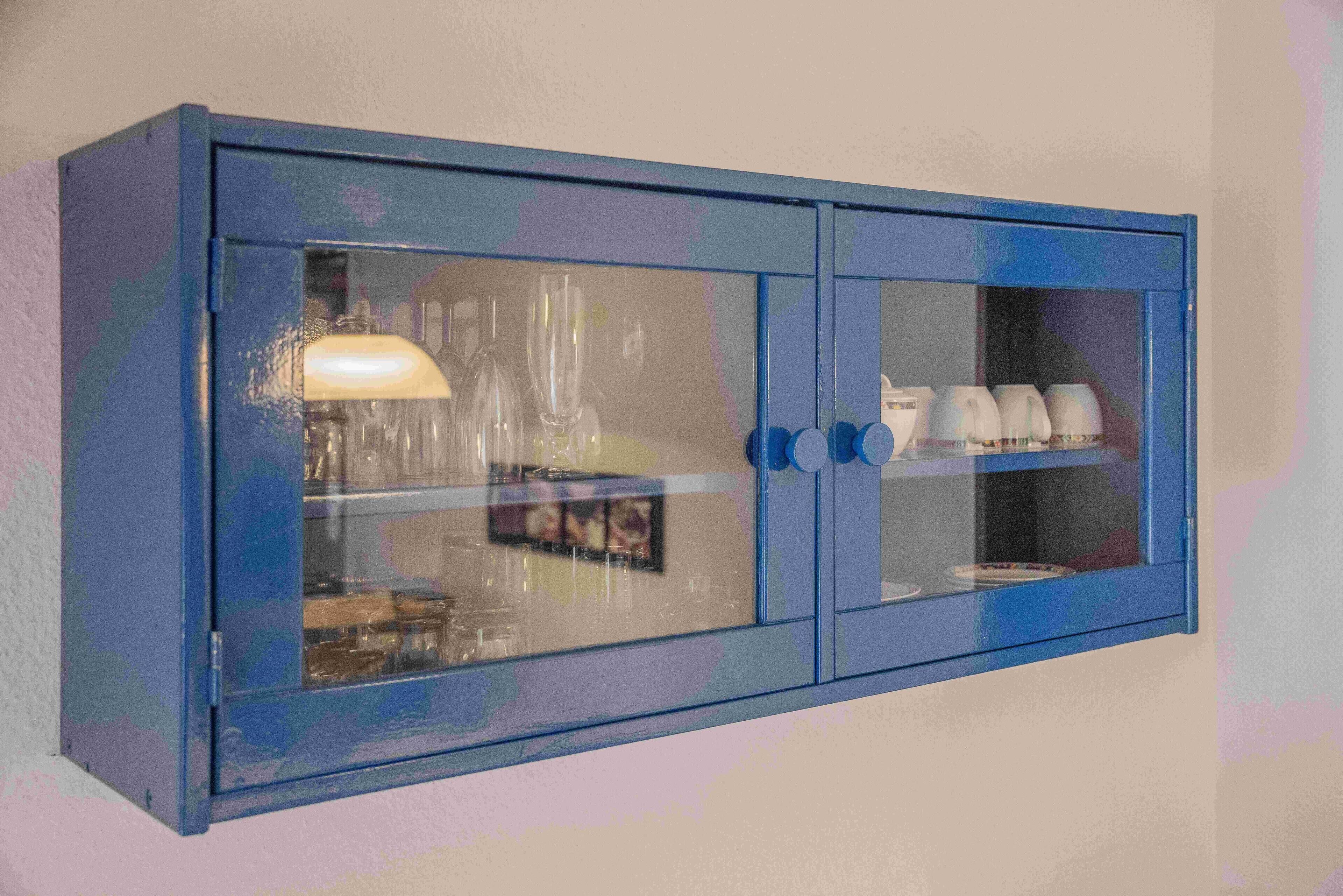 A blue cabinet with glass doors, containing various items like cups and a picture frame.
