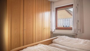 A bedroom with a wooden wardrobe, a window with a view of a brick building, and a radiator. - Just let your mind wander: the quiet location of this holiday Doppelha (Carolinensiel)
