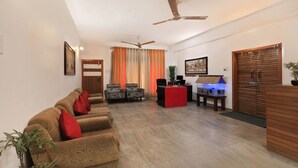 A living room with a sofa set, two patterned armchairs, a desk with a computer, a fish tank, and a ceiling fan. - Treebo Umal Homestay Ganeshguri (Guwahati)