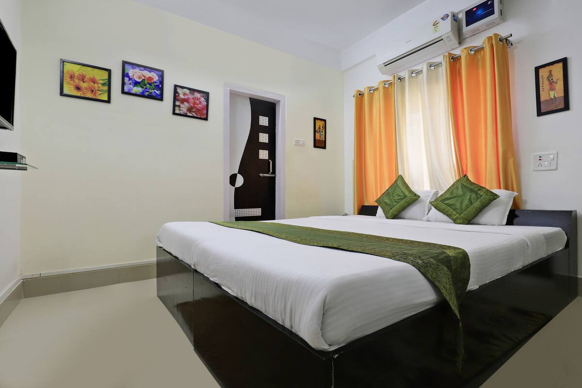 A hotel room with a large bed, a flat-screen TV, an air conditioning unit, and a door with a handle.