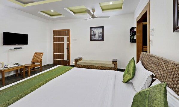 A hotel room with a bed, a chair, a small table, a television, a ceiling fan, and a door.