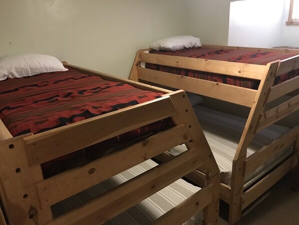 Two wooden bunk beds with red and black patterned bedding, a plain wall, and a window with natural light.
