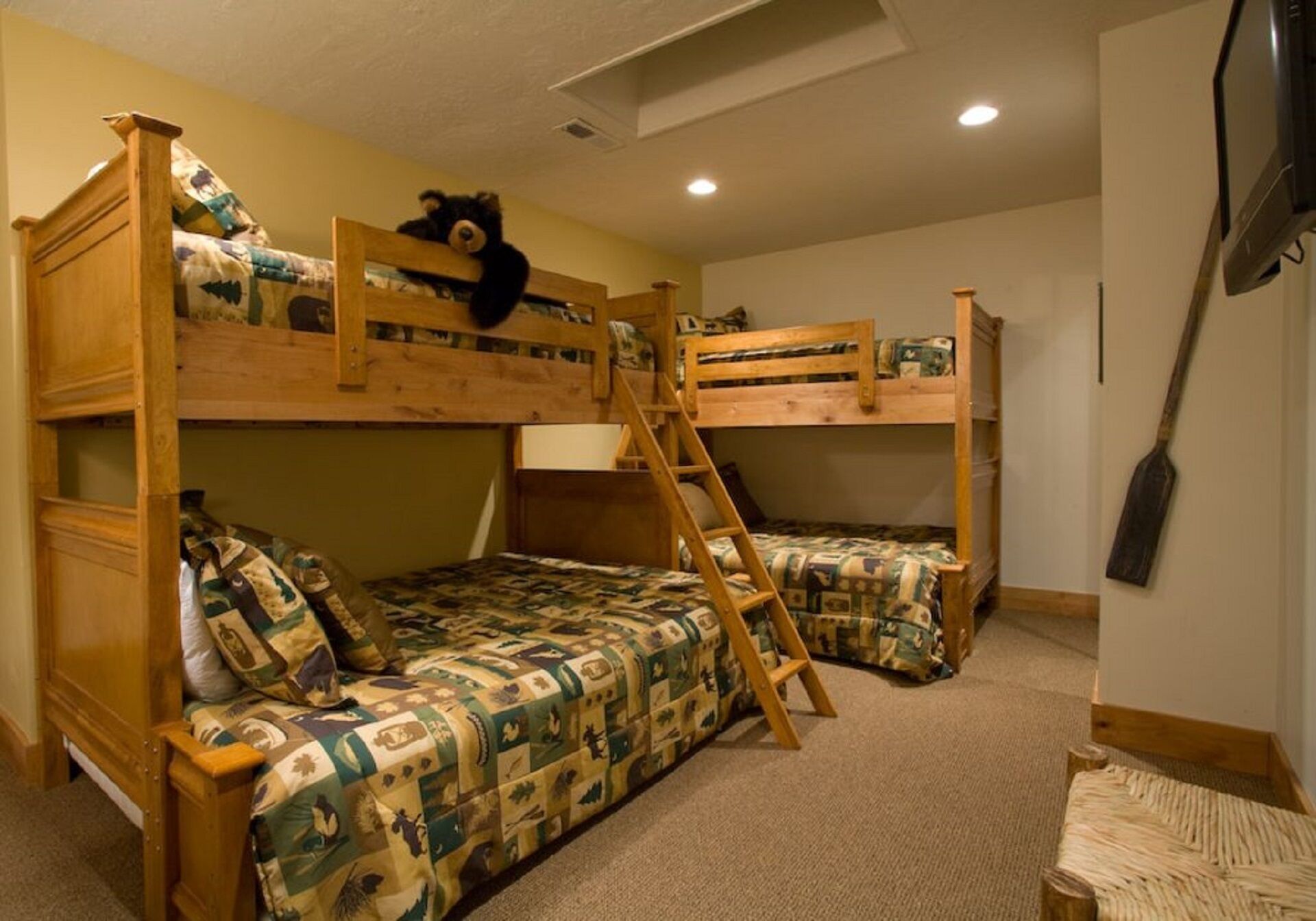 A bunk bed room with a ladder, a wooden chair, and a bear decoration.