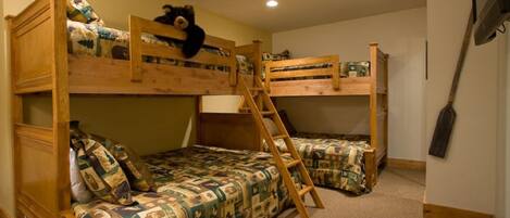 A bunk bed room with a ladder, a wooden chair, and a bear decoration.