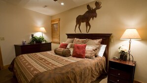 Ein Schlafzimmer mit einem großen Bett, zwei Nachttischen, einem Holzkopfteil und einer Wanddekoration mit einem Elch.