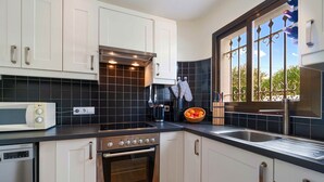 A modern kitchen with white cabinets, a black tiled backsplash, stainless steel appliances, and a window with decorative iron bars. - ASHANTI ZEN GARDEN DELUXE (ALTEA REGION) (La Nucia)