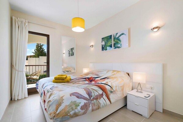 A bedroom with a bed, bedside table, and a window with curtains.