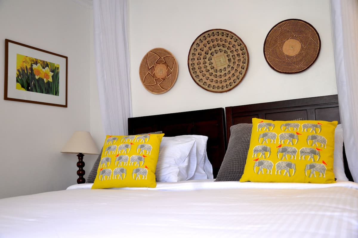 A hotel room with a neatly made bed, two pillows with elephant designs, and three woven wall hangings.