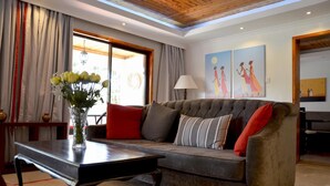 A living room with a grey sofa, red and striped pillows, a vase with flowers, and a table. There are two paintings on the wall and a lamp on a side table. - Villa Machakos Hotel and Conferencing (Machakos)