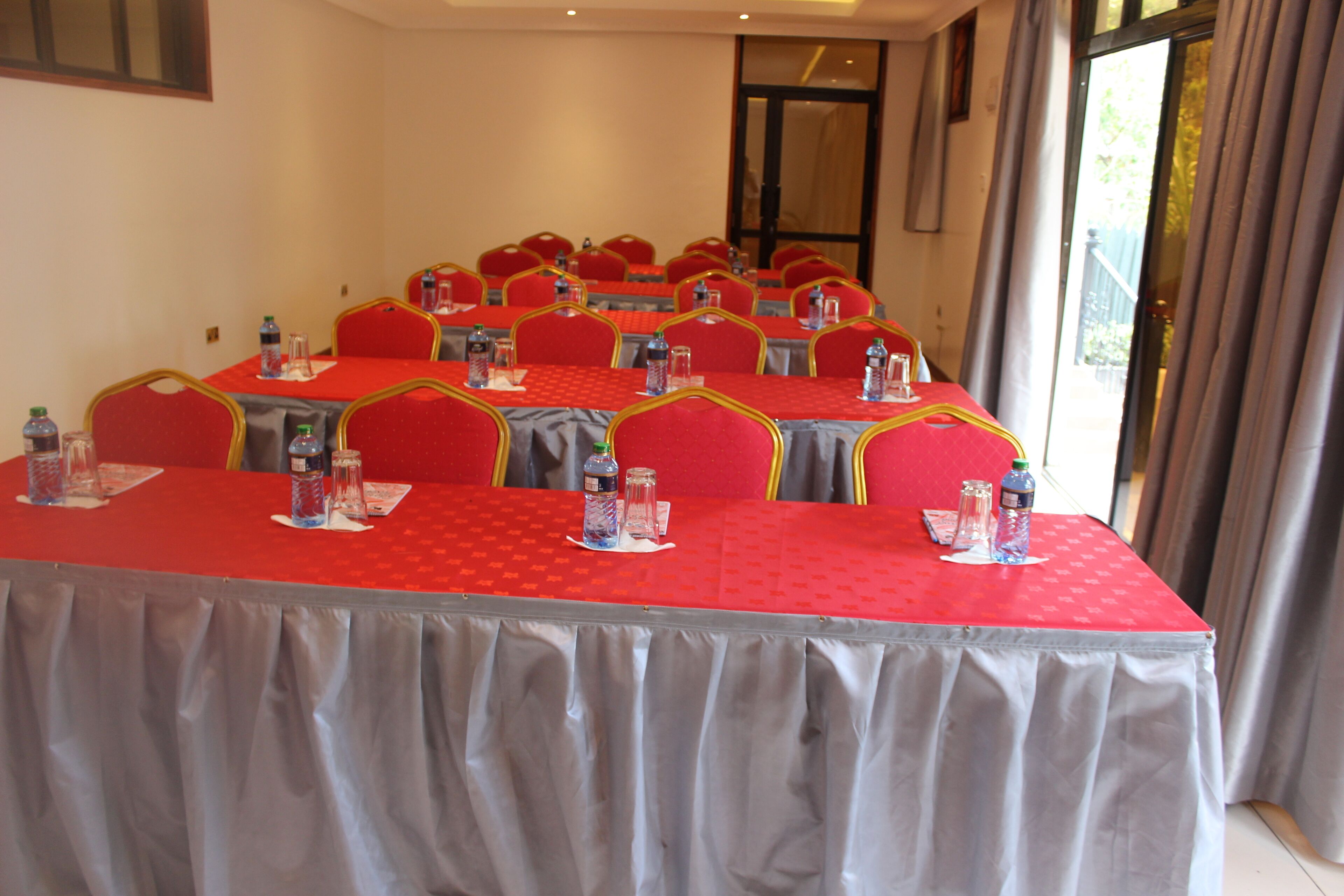 A conference room with multiple tables, each with red tablecloths, chairs, and water bottles.