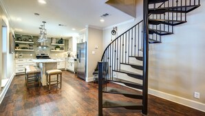 A modern kitchen with a central island, stainless steel appliances, and a black spiral staircase.
