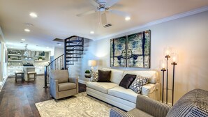 A spacious living area with a sofa set, a patterned rug, and a modern kitchen in the background.