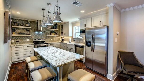 A modern kitchen with white cabinetry, a stainless steel refrigerator, and a marble island with bar stools.