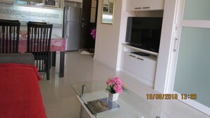 A modern kitchen with white cabinets, a refrigerator, microwave, and a dining area with a table and chairs. - SUPER 404 LUXURY APARTMENT, QUIET, IN THE DINAMIQUE DISTRICT OF JOMTIEN. (Jomtien)