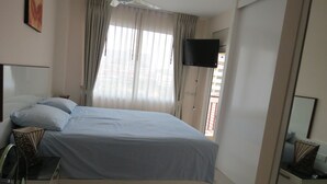 A hotel room with a bed, a TV mounted on the wall, and a window with curtains. - SUPER 404 LUXURY APARTMENT, QUIET, IN THE DINAMIQUE DISTRICT OF JOMTIEN. (Jomtien)